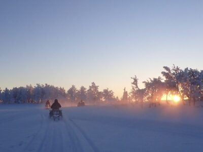 People on snowmobiles in Sweden. Bright blue sky and crisp white snow connected with a lining of silhouetted trees
