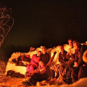 A group of people on the Arctic-Style Survival Challenge huddled around a fire smiling at the camera.